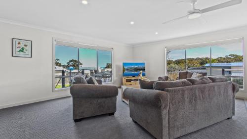 a living room with couches and chairs and windows at Pelican House - Modern Family Retreat in Lakes Entrance