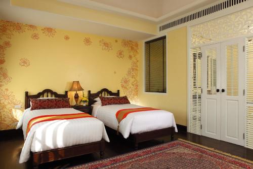 two beds in a bedroom with yellow walls at Ping Nakara Boutique Hotel And Spa in Chiang Mai