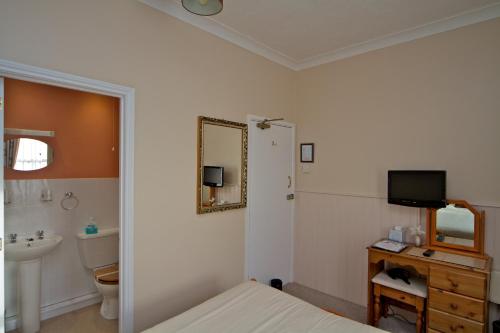 uma casa de banho com uma cama, um lavatório e um espelho. em Cornubia Guest House em Weymouth