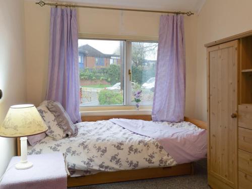 1 dormitorio con 1 cama con cortinas moradas y ventana en Richmond Cottage en Ashby Saint Ledgers