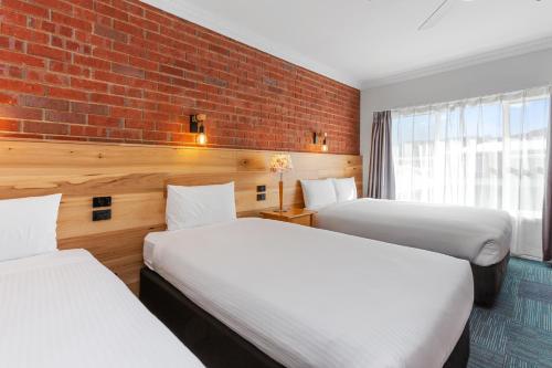 two beds in a room with a brick wall at The International Motel Apollo Bay in Apollo Bay