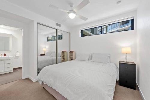 a white bedroom with a bed and a mirror at Lovely 2 Bedroom unit Pool,Gym workspace & more in Brisbane