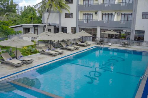 a swimming pool in front of a hotel with chairs and umbrellas at Hotel Comster Mtwapa in Mtwapa