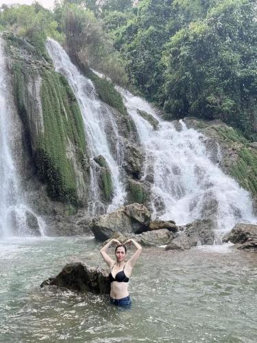 a woman standing in the water in front of a waterfall at Mai Chau Xanh Bungalow in Mai Chau