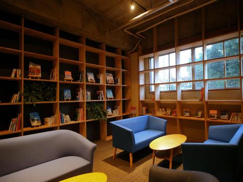 TRAVEL&BOOK HOTEL HULATONCABIN TAKAMATSU في تاكاماتسو: مكتبة بها كرسيين وطاولة وأرفف كتب