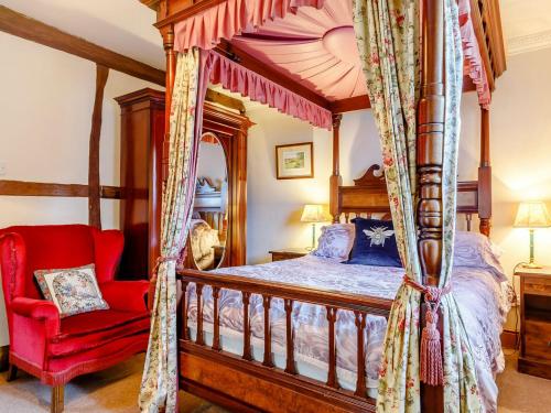 a bedroom with a canopy bed and a red chair at The Pigsty - Uk30945 in Barthomley