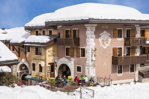 un grand bâtiment avec des personnes debout à l'extérieur dans la neige dans l'établissement Hôtel du Bourg, à Valmorel