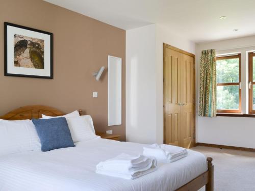 a bedroom with a bed with white sheets and a window at Battanropie Lodge in Carrbridge