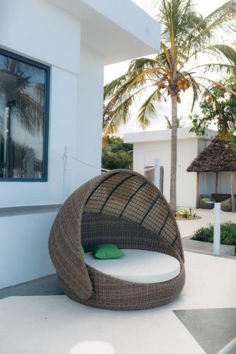 a rattan bed on a patio with a palm tree at Safira Blu Luxury Resort & Villas in Nungwi