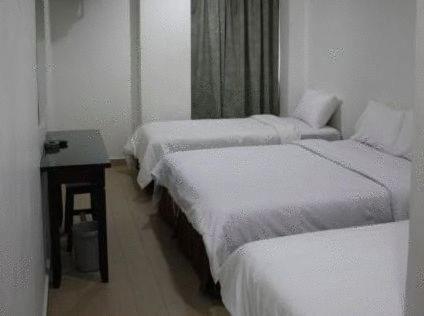 a row of three beds in a room with a table at Dynasty Inn - Wakaf Che Yeh in Wakaf Che Yeh