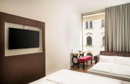 a hotel room with a couch and a television on a wall at elaya hotel leipzig city center in Leipzig