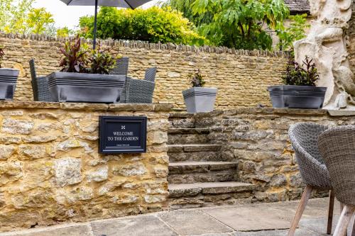 a stone wall with potted plants and a sign on it at The Unicorn (Apartments) in Stow on the Wold
