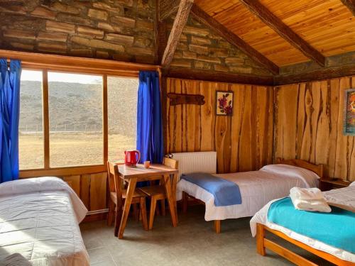 a bedroom with two beds and a table and a window at Hostería & Cabañas Río Fénix in Perito Moreno