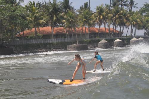 dos chicas montando una ola en una tabla de surf en el agua en Surfers Villa and Resorts Medewi, en Jembrana