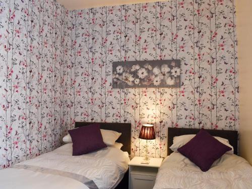 two beds in a room with floral wallpaper at End Cottage in Alnwick