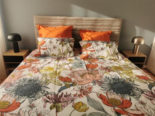 a bed with a floral comforter and orange pillows at La Maison de Lucie - grande maison idéale en famille ou entre amis - jardin - parking gratuit in Sélestat