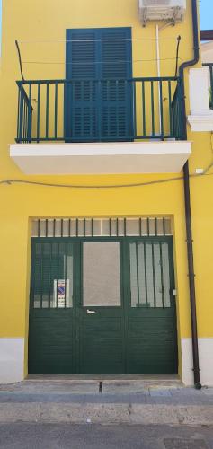 a yellow building with a green garage door and a balcony at Casa Vacanza a Punta Secca in Punta Secca