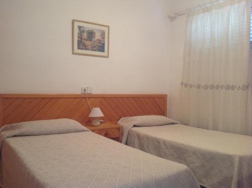 two beds in a hotel room with a window at Apartamentos Can Miguel in Cala San Vicente