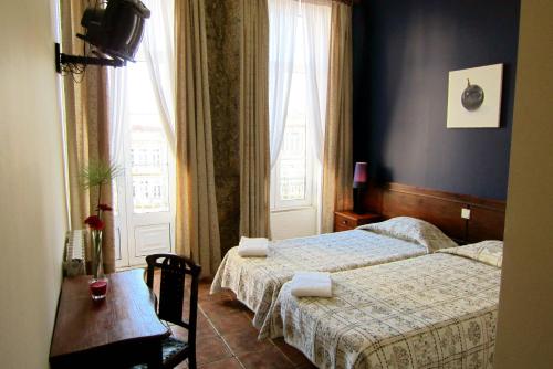 a bedroom with two beds and a table and a window at Duas Nações Guest House in Porto