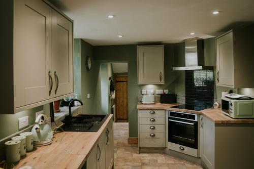 a kitchen with green walls and white cabinets at White Side Cottage in Haltwhistle