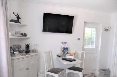 a white room with a table and a television on the wall at THE KNIGHTWOOD OAK a Luxury King Size En-Suite Space - LYMINGTON NEW FOREST with Totally Private Entrance - Key Box entry - Free Parking & Private Outdoor Seating Area - Town ,Shops , Pubs & Solent Way Walking Distance & Complimentary Breakfast Items in Lymington