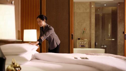 a woman standing over a bed in a hotel room at InterContinental Kunming by IHG in Kunming
