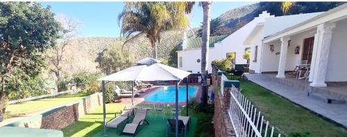 a house with a swimming pool and an umbrella at De Oude Meul Country Lodge & Restaurant in Oudtshoorn
