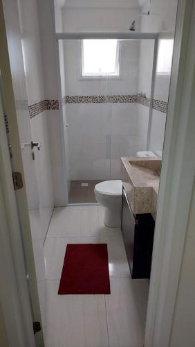 a white bathroom with a toilet and a red rug at Apartamento Praia Grande -Canto do Forte in Praia Grande