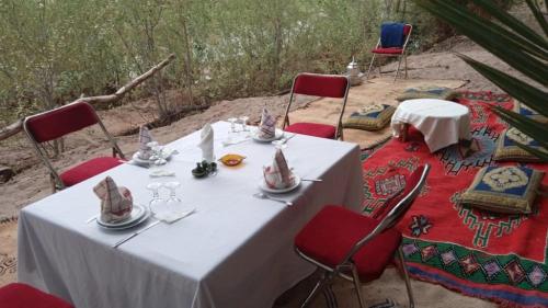 a table with red chairs and a white table with glasses at Auberge Restaurant TISSILI " Oasis de Fint" in Fint