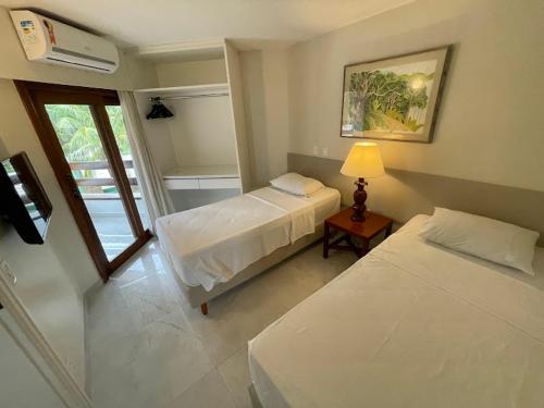 1 dormitorio con 2 camas, lámpara y ventana en Flat no Hotel Jatiúca suítes resort en Maceió