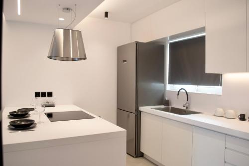 a white kitchen with a stainless steel refrigerator at Seafront Apartment by C2C Architects in Kalívia Thorikoú