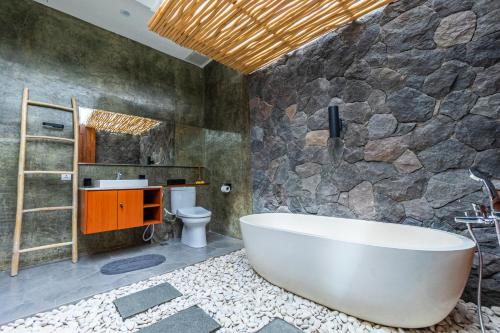 a bathroom with a large tub and a stone wall at Villa Sokhaya in Ubud