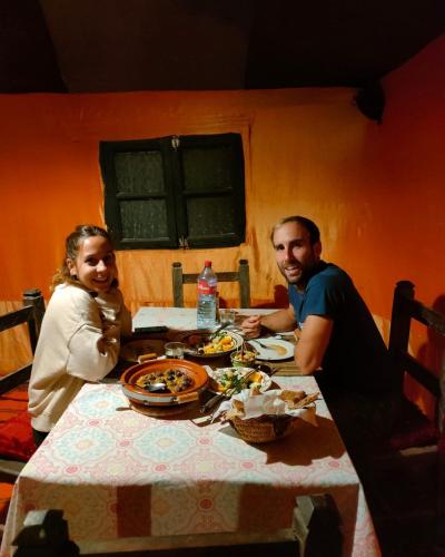 a man and a woman sitting at a table with food at Overnight Desert Camp in Merzouga