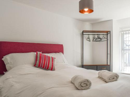 a bedroom with a white bed with a red headboard at Chuckle Cottage in Braunton