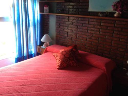 1 dormitorio con cama roja y pared de ladrillo en VILLA GESELL Departamento Frente al Mar en Villa Gesell