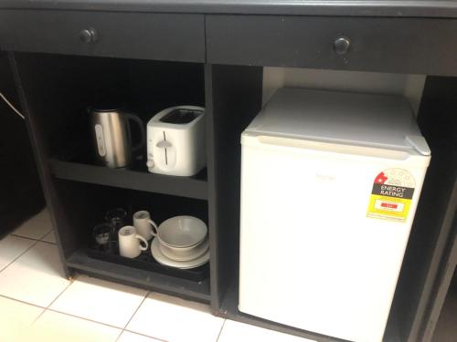 a kitchen cabinet with a shelf with dishes and a refrigerator at Matador Motor Inn in Coffs Harbour