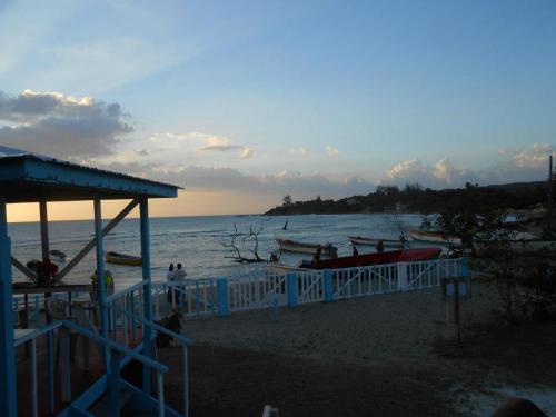 a beach with boats in the water and a blue fence at Waikiki Guest House in Treasure Beach