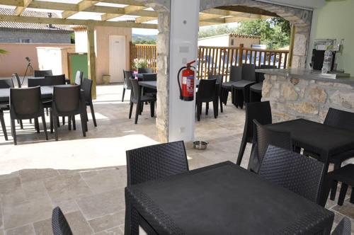 un restaurante con mesas y sillas negras y un patio en Camping Chalets Les Chênes Verts, en Vogüé