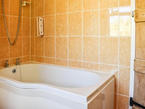 a bath tub in a bathroom with a tile wall at Tansey Cottage in Hartlebury