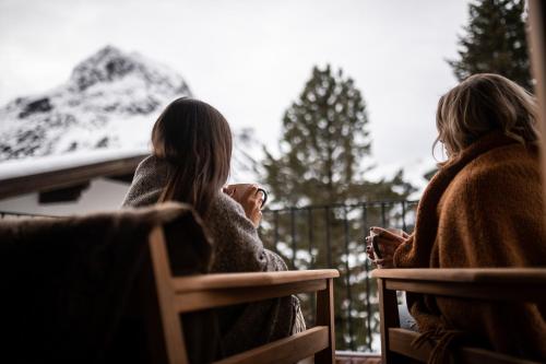 two women sitting on a balcony looking at a snow covered mountain at Arla Luxury Home in Lech am Arlberg