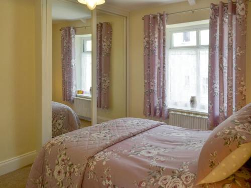 a bedroom with a pink bed and a mirror at Dollys Cottage in Ovingham
