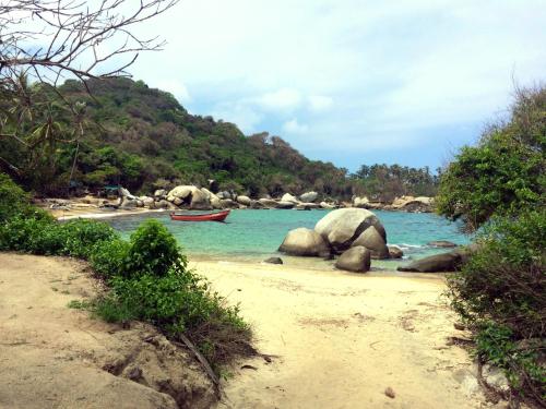 a beach with rocks and a boat in the water at Tayrona Tented Lodge in Guachaca