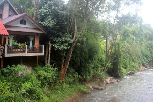 a house with a balcony next to a river at Little Eden Guesthouse in Pang Mapha