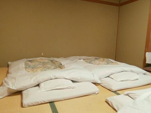 ein Bett mit weißer Bettwäsche und Kissen darauf in der Unterkunft Hoshikawakan in Yamanouchi