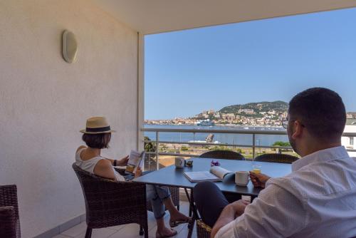 dwie osoby siedzące przy stole z widokiem na ocean w obiekcie Residence de Tourisme Ajaccio Amirauté w Ajaccio
