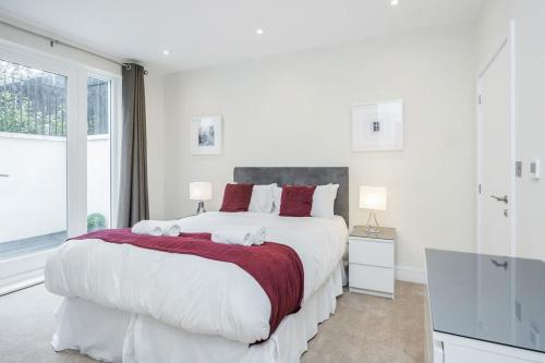 a white bedroom with a large bed with red pillows at Roomspace Serviced Apartments - Lockwood House in Surbiton