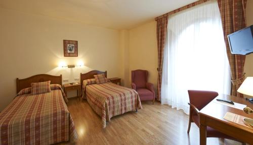 a hotel room with two beds and a desk at Hotel Abat Cisneros Montserrat in Montserrat