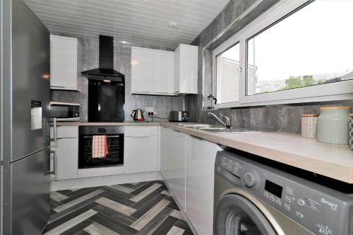 a kitchen with white cabinets and a washer and dryer at Signature - Carnoustie House in East Kilbride