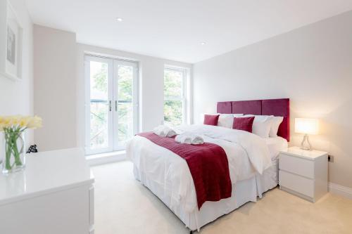 a white bedroom with a large bed and windows at Roomspace Serviced Apartments - Trinity House in Reigate
