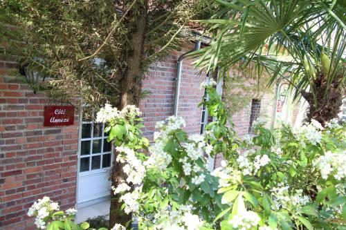 un bâtiment en briques avec des fleurs blanches devant une porte dans l'établissement Les Jardins Carnot, à Compiègne